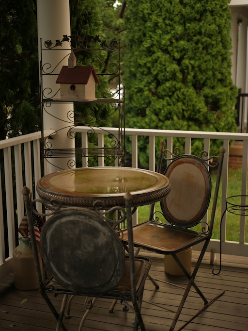 A metal chair on a porch after a rain, basking in a warm glow.